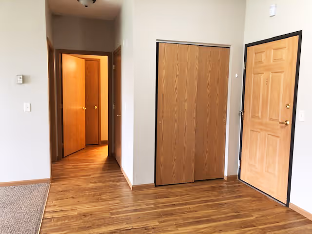 Entryway with a front door, wood flooring, a closet with sliding wooden doors, and a hallway leading to open interior doors.