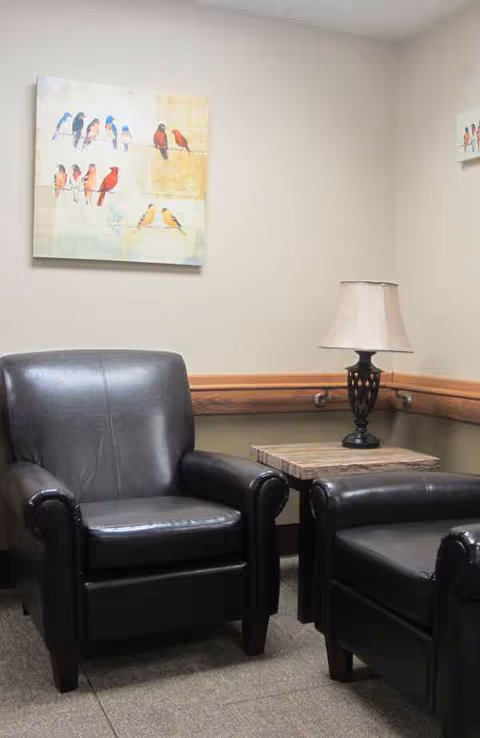 Two black leather chairs flank a small table with a lamp in a neutral lounge.