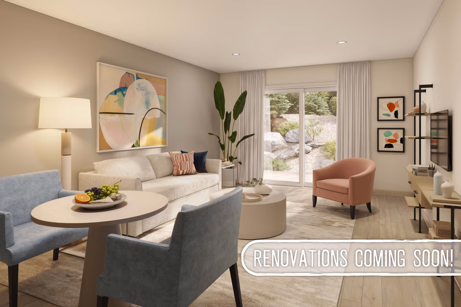 A modern living room with a beige sofa, two blue armchairs around a round table with fruit, a pink armchair, a round coffee table, a floor lamp, abstract wall art, and large sliding glass doors leading to an outdoor garden area.