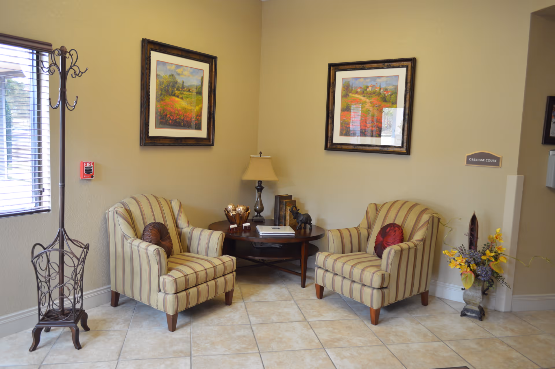A reception-style seating area with two striped armchairs, a round wooden table with a lamp and framed artwork on the wall.