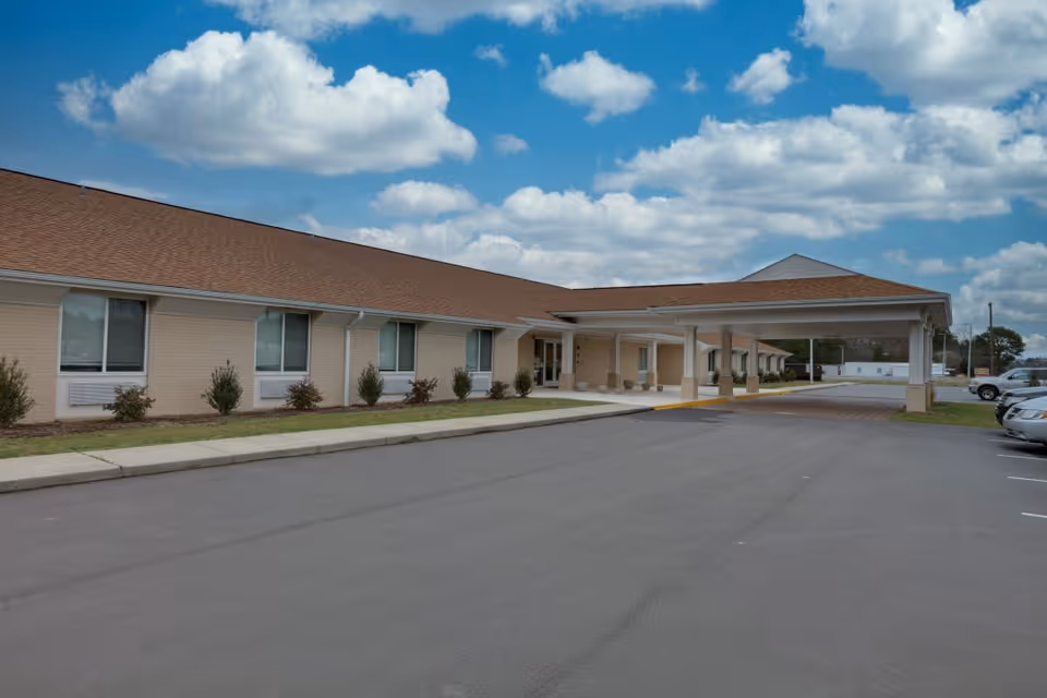 Single-story senior living building with a covered entrance and parking lot under a blue sky.