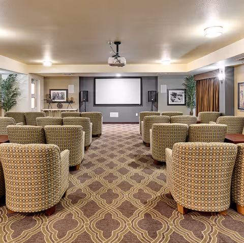 A small media room with rows of upholstered armchairs facing a projection screen and speakers.