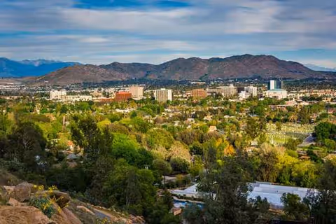 A scenic valley view of a city with buildings, trees, and distant mountains.