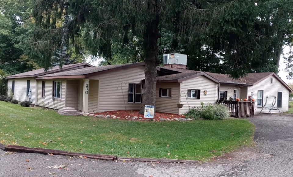 One-story beige building with a large tree in front and a small wooden deck