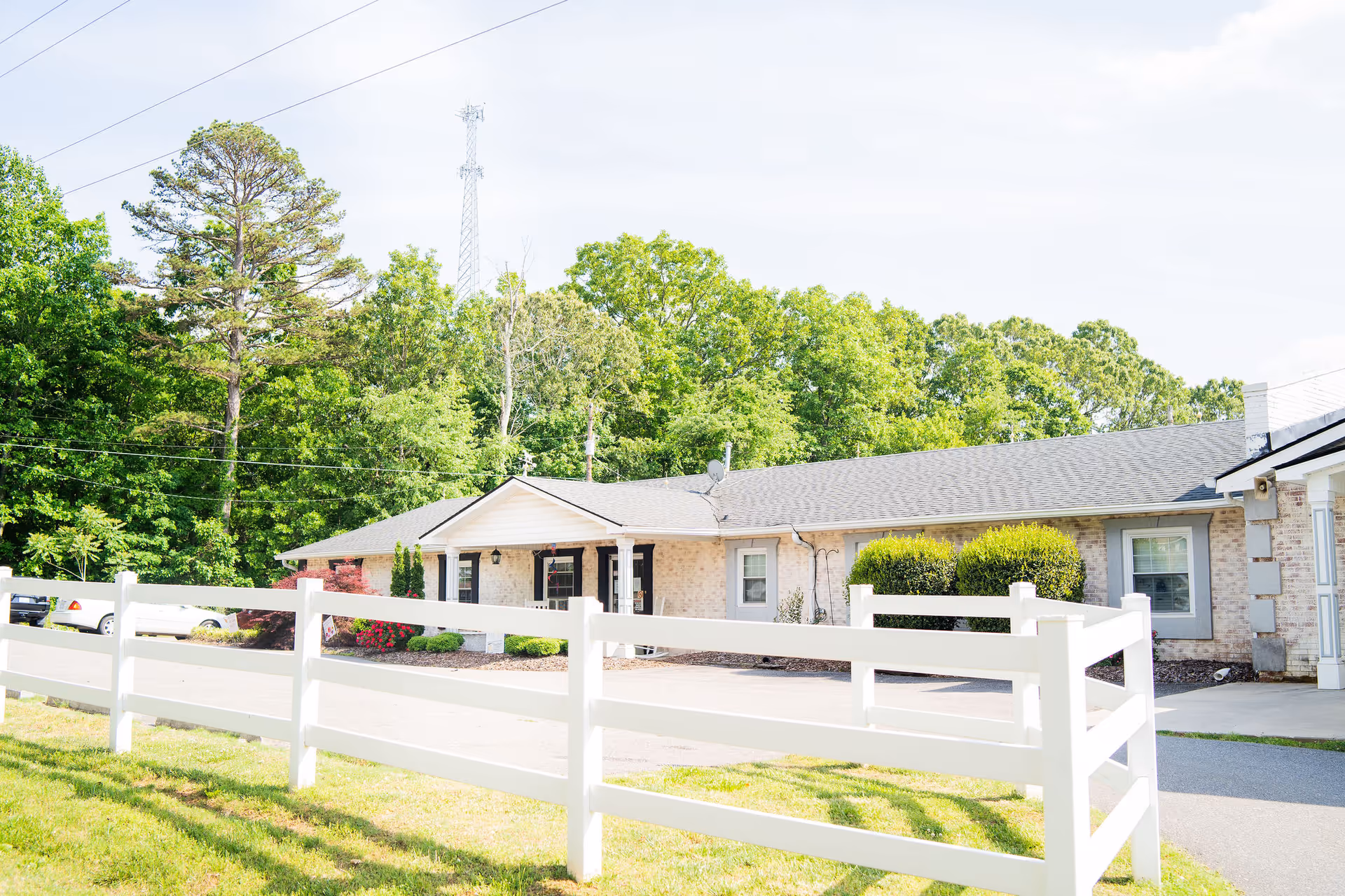 Single-story brick memory care building with a white fence in front and trees behind.