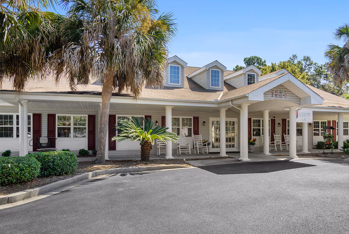 A single-story senior living facility with a covered front porch and white rocking chairs.