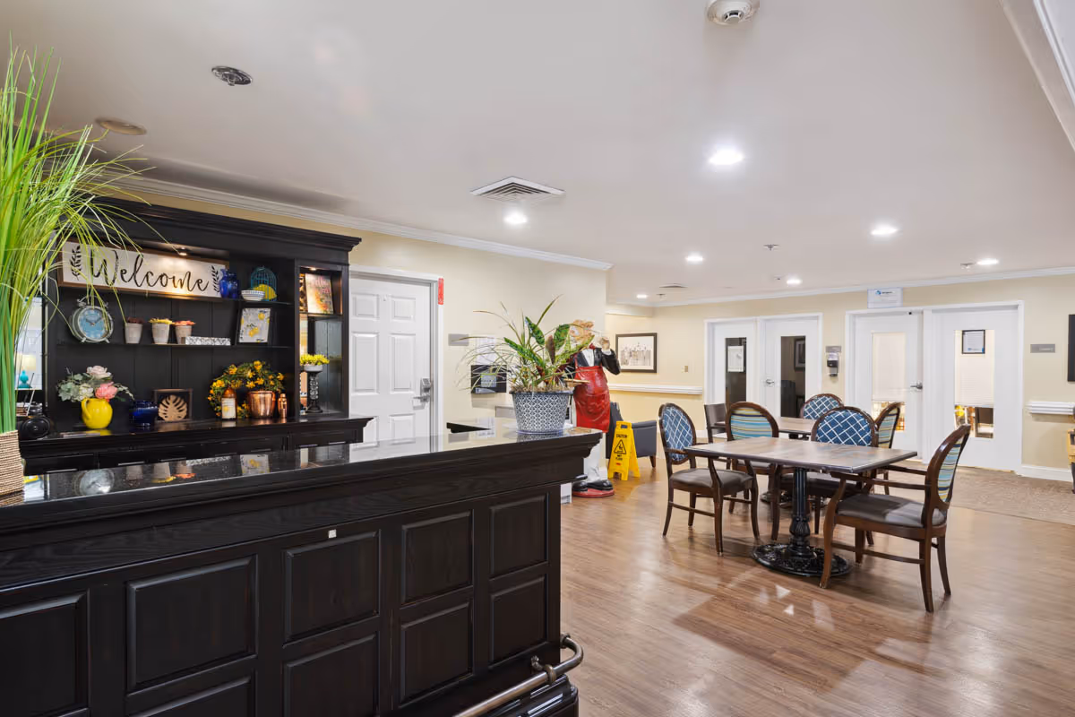 Reception/common area with a dark wooden front desk, decorative shelving with a 'Welcome' sign, and a table and chairs seating area.
