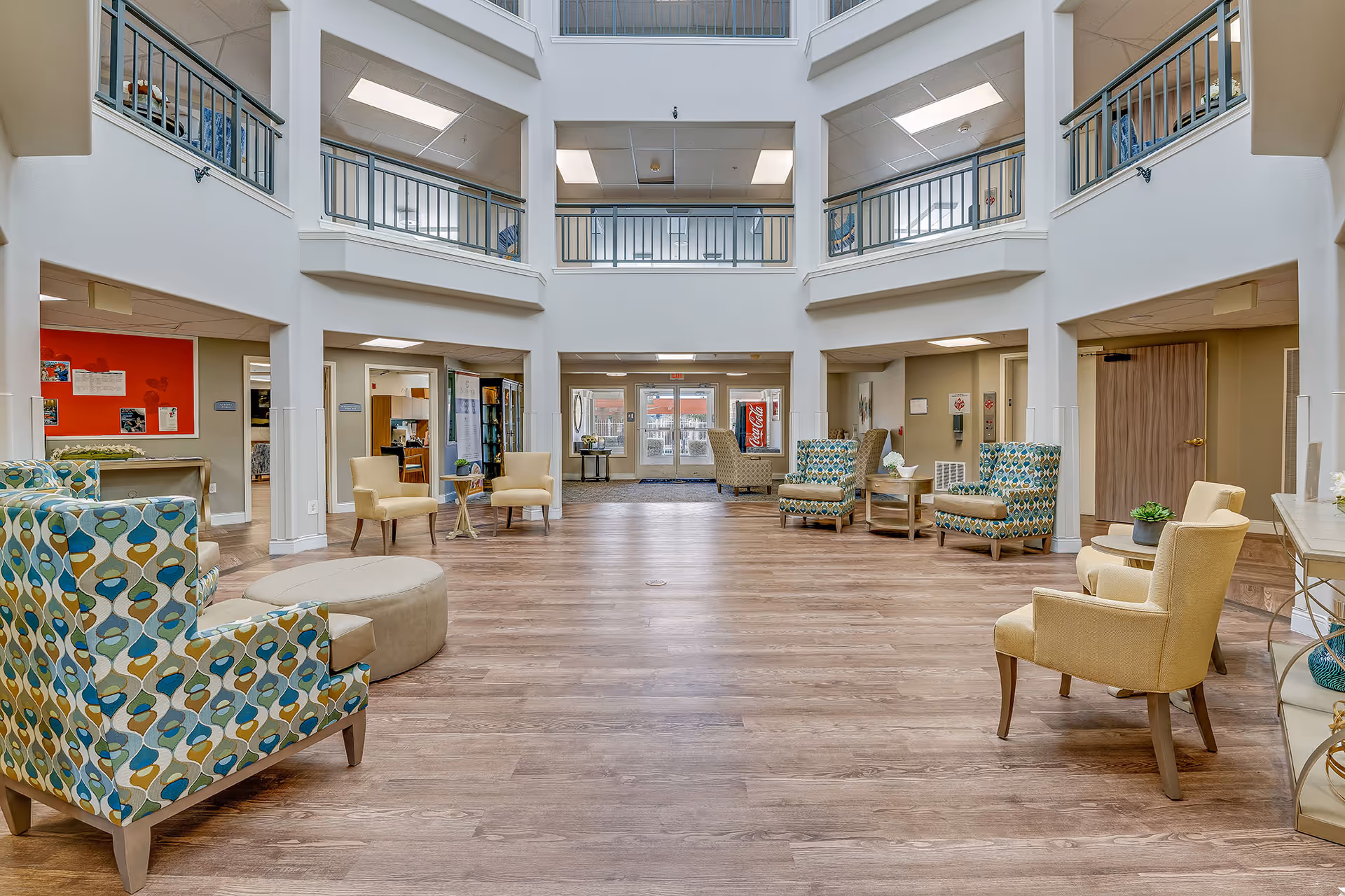 Bright multi-level atrium lounge with patterned armchairs, seating clusters, and wood flooring.