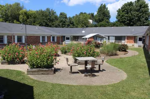 Single-story brick senior living building surrounds a circular outdoor courtyard with benches and flowers.