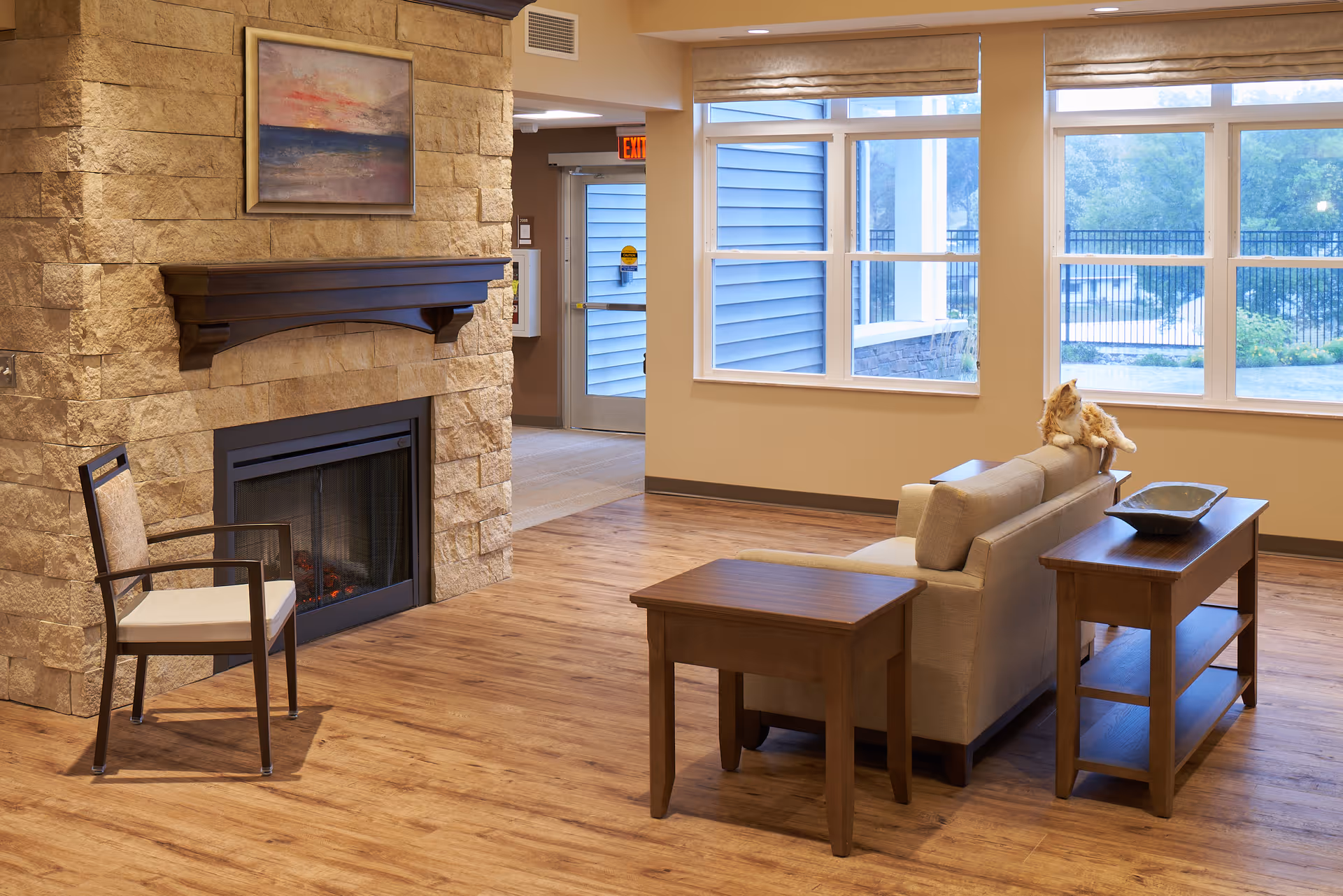 Bright common living area with a stone fireplace, sofa and wooden tables in front of large windows.
