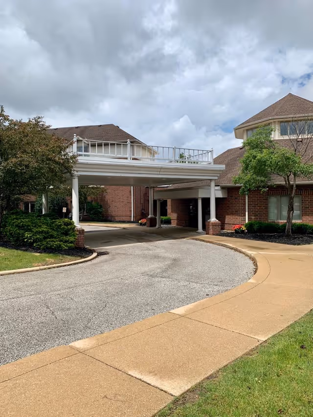Covered entrance drive and porte-cochere at a brick senior living facility with landscaping under a cloudy sky.