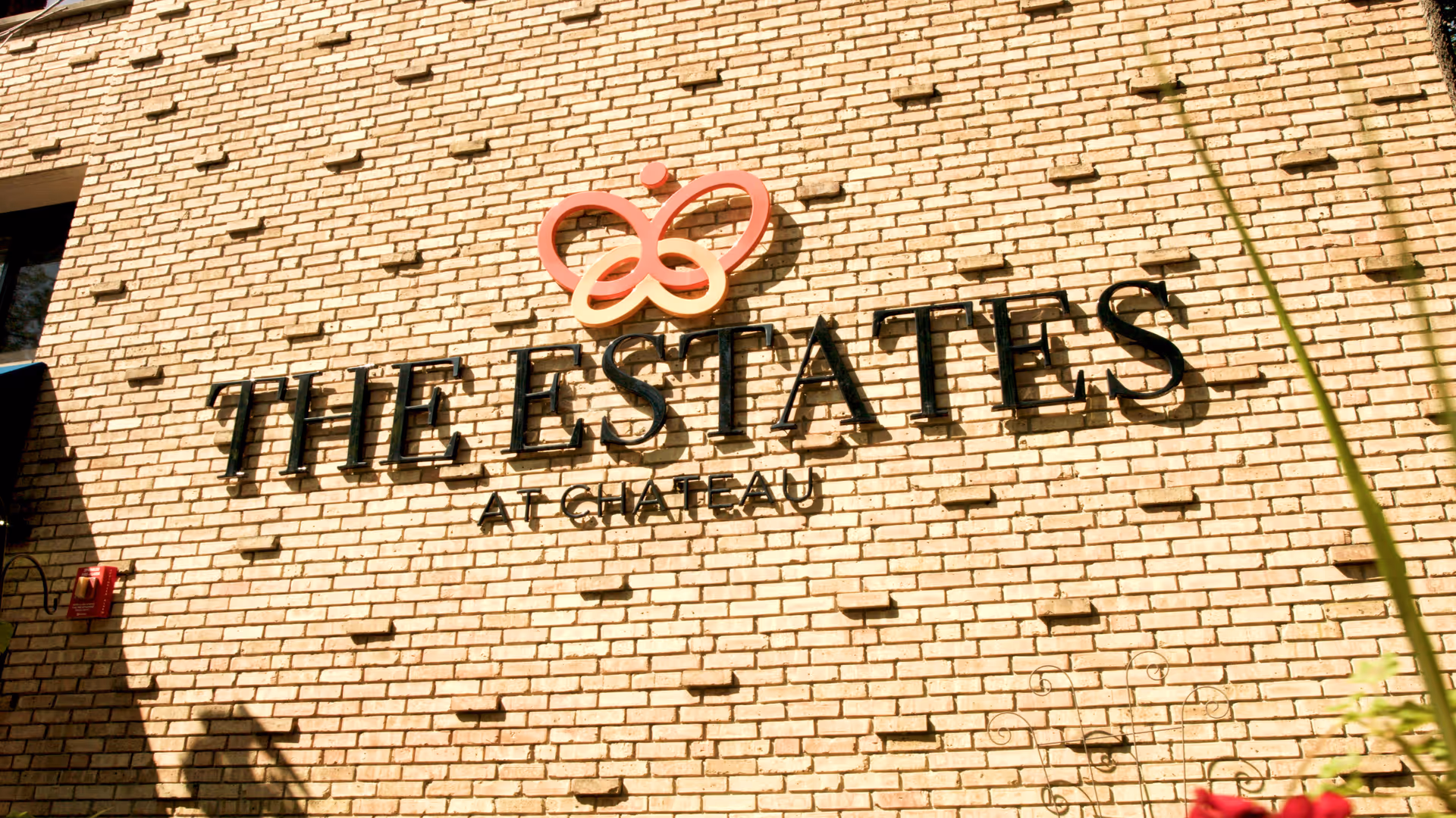 Exterior brick wall with a sign that reads 'THE ESTATES AT CHATEAU' featuring a butterfly logo above the text.