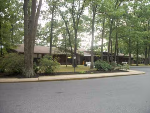 Exterior view of a senior living facility with trees and a curved driveway.
