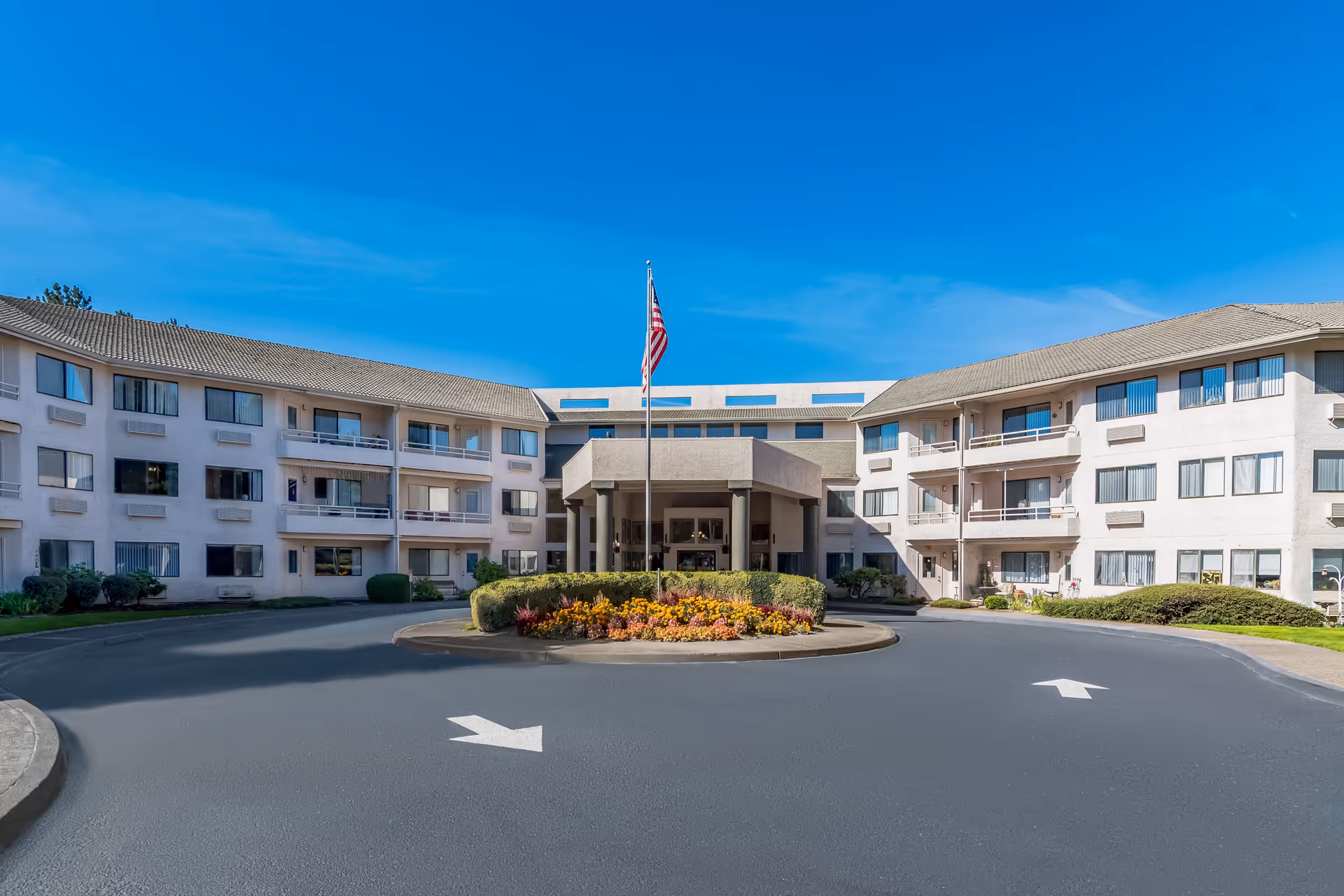 Front view of a senior living facility with a circular driveway and flagpole