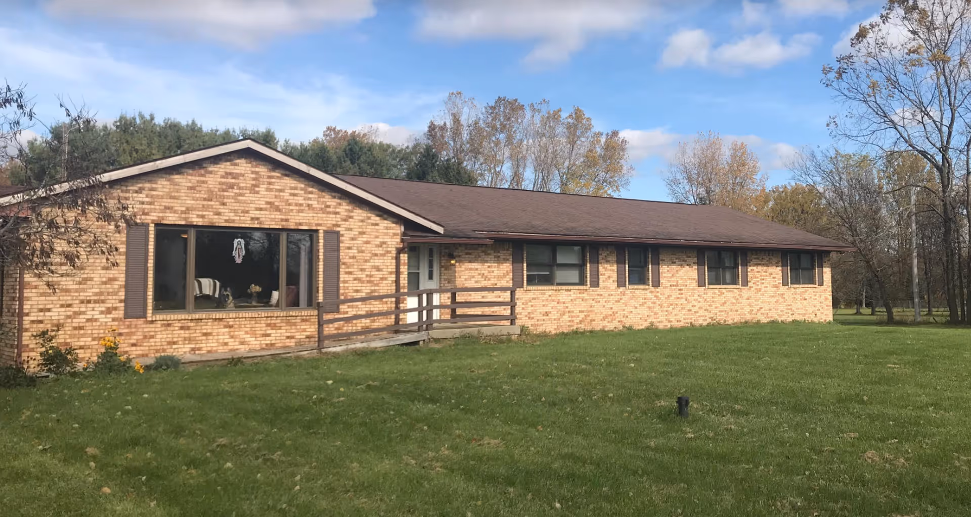 Single-story brick ranch-style building with a ramped entrance, large front window and a grassy lawn under a partly cloudy sky.