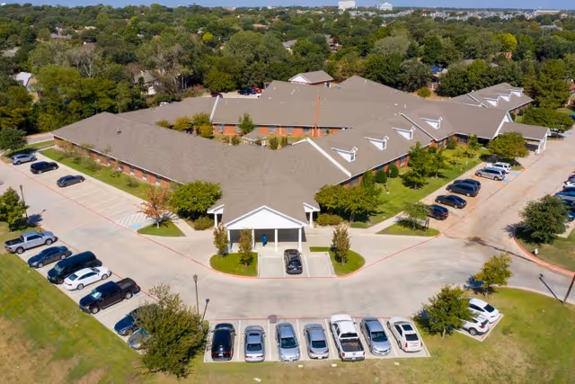 Aerial view of a single-story senior living building with a covered main entrance, surrounding parking lots, and landscaped grounds.