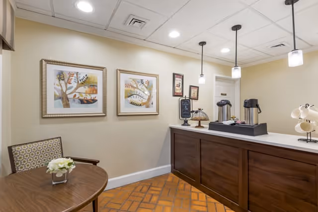 Small coffee station and seating area with a wooden counter, pendant lights, and framed artwork on the wall.