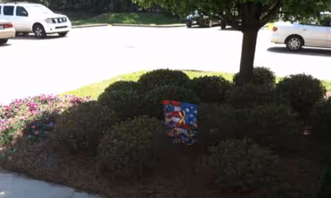 A landscaped parking lot median with trimmed bushes and a small sign.