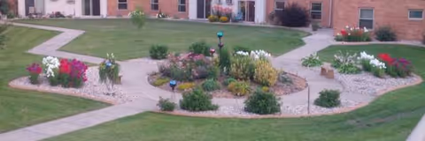 Well-kept front courtyard garden with circular flower beds and a brick building backdrop.