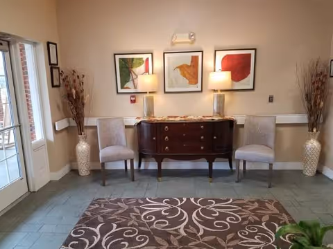 Elegant lobby seating area with two gray chairs, a dark console, lamps, and abstract art.