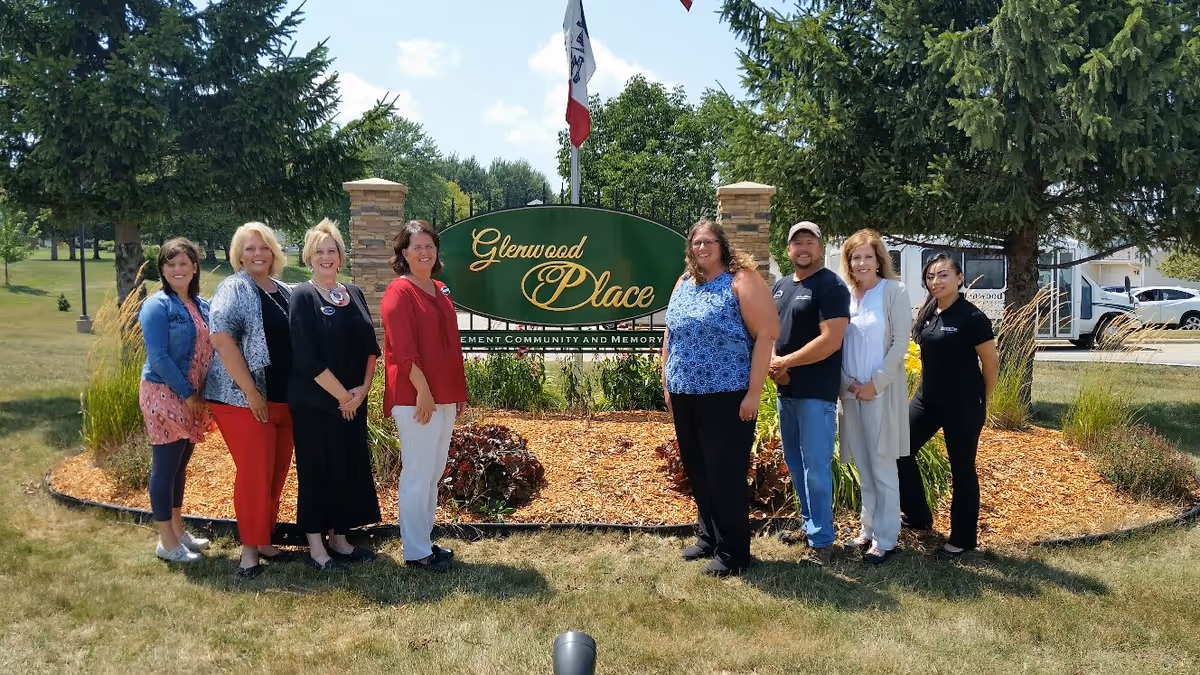 A group of staff members standing outdoors in front of a landscaped sign that reads 'Glenwood Place'.