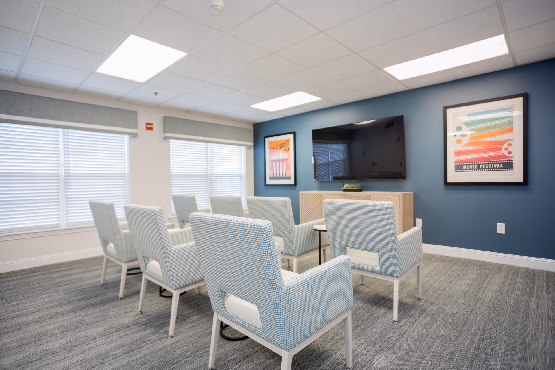 Small media room with light blue armchairs arranged facing a wall-mounted TV and framed artwork.