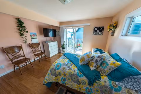 Bright pink-walled bedroom with a bed, dresser, chairs, and a sliding door to a balcony.
