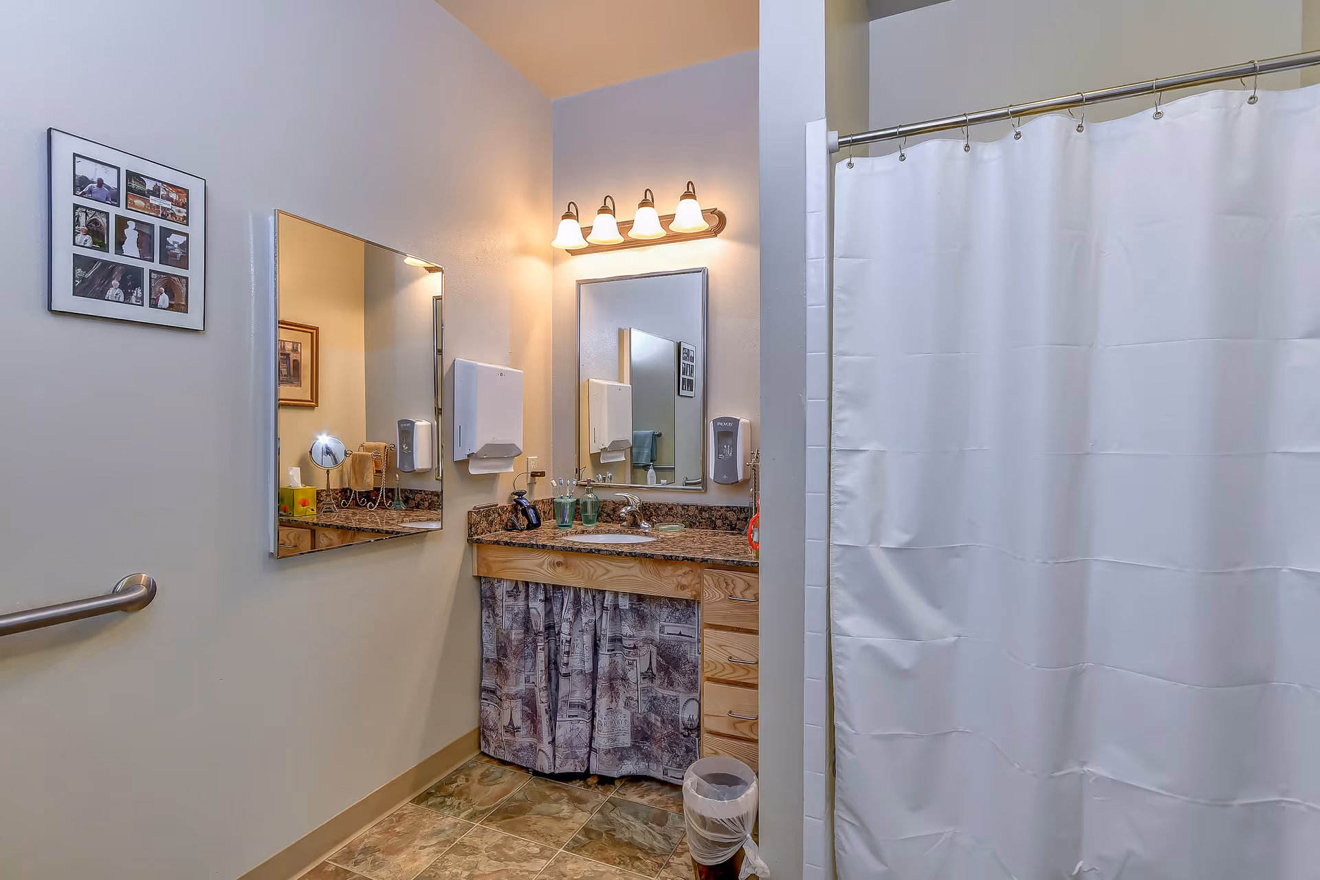 Bathroom with a vanity and mirror, soap dispensers and a sink next to a shower with a white curtain.