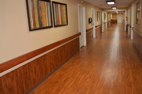 Long wood-floored interior hallway with handrails, framed artwork, and closed doors.