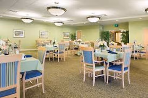 A pastel dining room in a senior living facility with arranged tables and chairs.