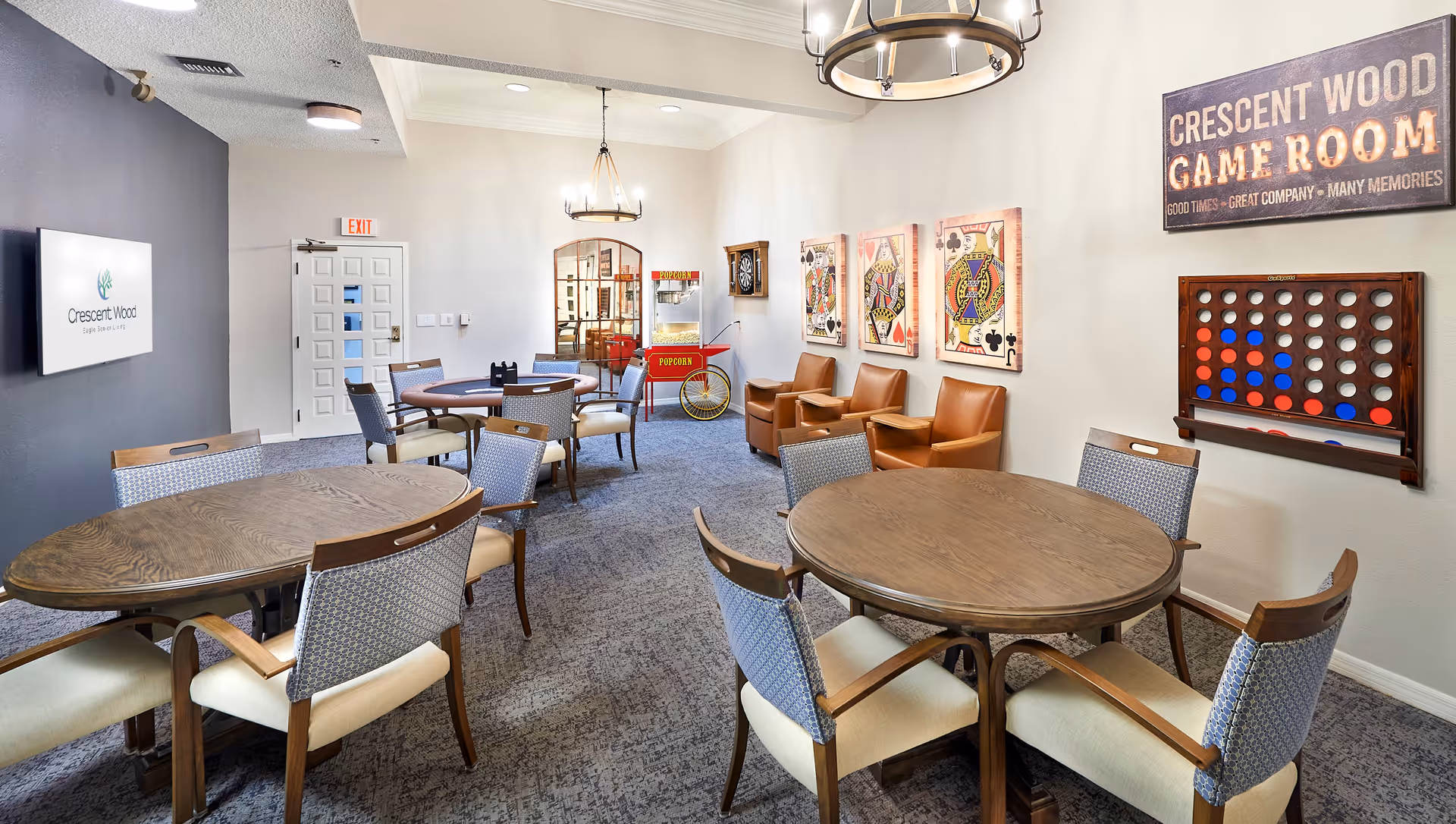 Well-lit Crescent Wood game room with round tables and chairs, lounge seating, wall games and a popcorn cart.