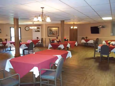 Retirement center dining room with red tablecloths and arranged chairs.