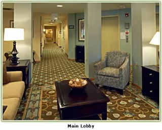 A furnished main lobby with armchairs, a coffee table, lamps, and a long carpeted hallway.