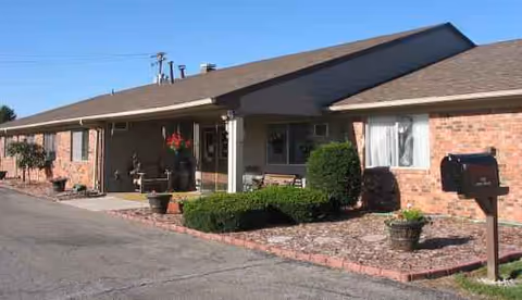 Single-story brick senior living facility exterior with shrubs and potted plants.