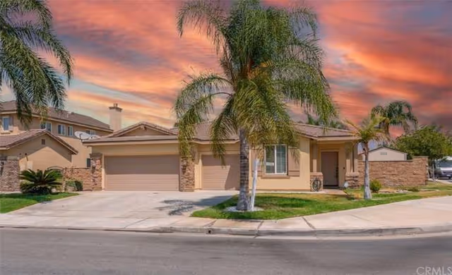 Single-story stucco house with palm trees, a three-car garage and a colorful sunset sky.