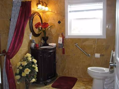 Small bathroom with sink vanity, toilet, window, and burgundy decorative accents.