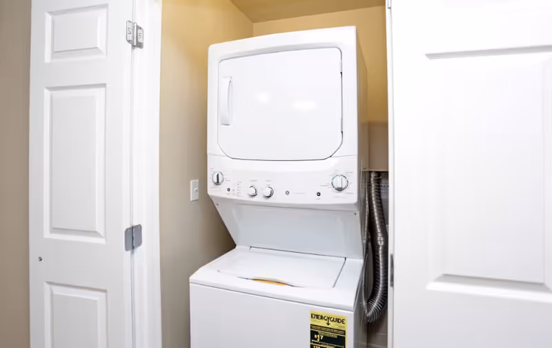 A stacked washer and dryer unit installed in a small laundry closet with the doors open.