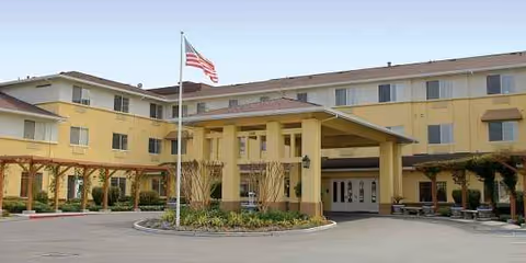 Exterior view of Carlton Senior Living San Jose building, entrance canopy, and flag