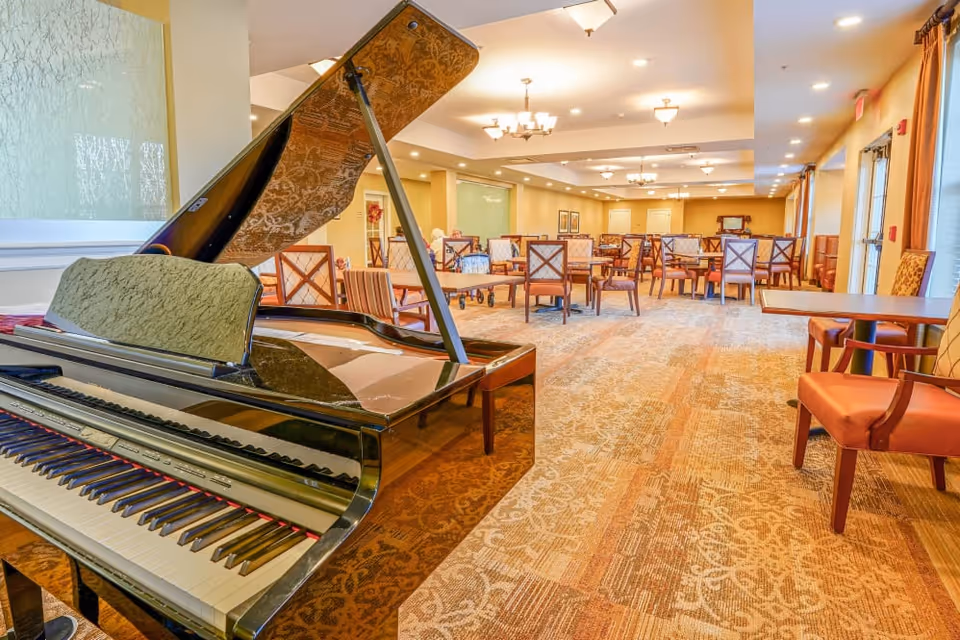 Grand piano in a spacious dining/activity room with multiple tables and chairs.