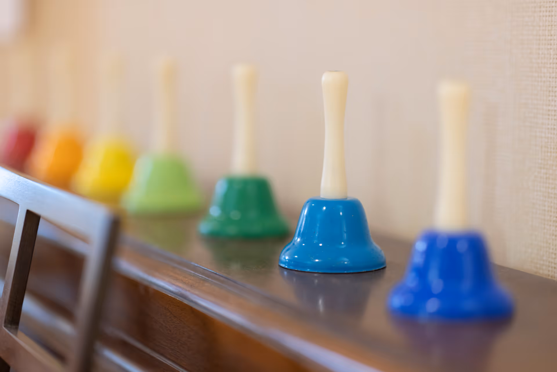 A row of small colorful handbells lined up on a wooden surface with a blurred background.