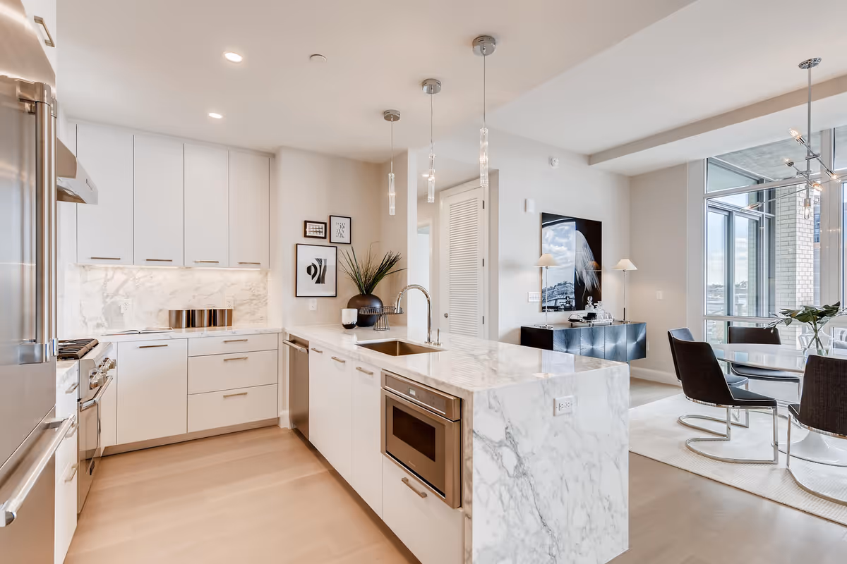 Bright modern kitchen with a marble island, stainless-steel appliances and an adjoining dining area with floor-to-ceiling windows.