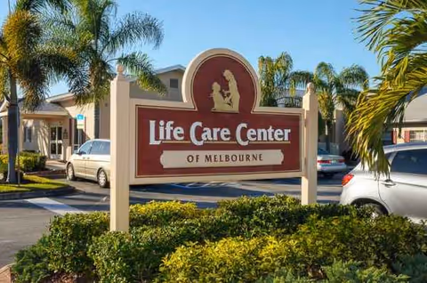 Front view of Life Care Center of Melbourne sign with palm trees and parked cars.