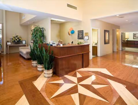 A spacious lobby with a wooden reception desk, star-patterned floor, and potted plants.