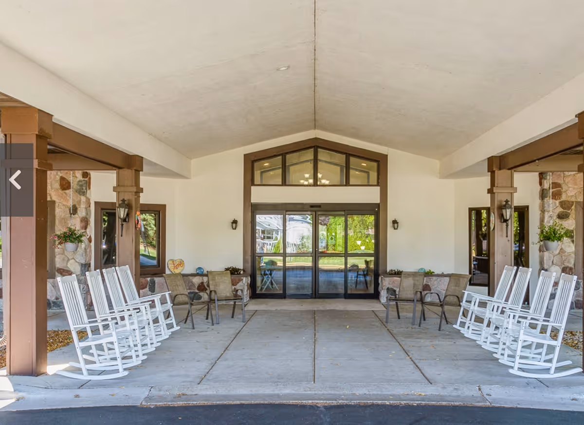 Covered main entrance with rows of white rocking chairs flanking a glass double door under a pitched canopy.