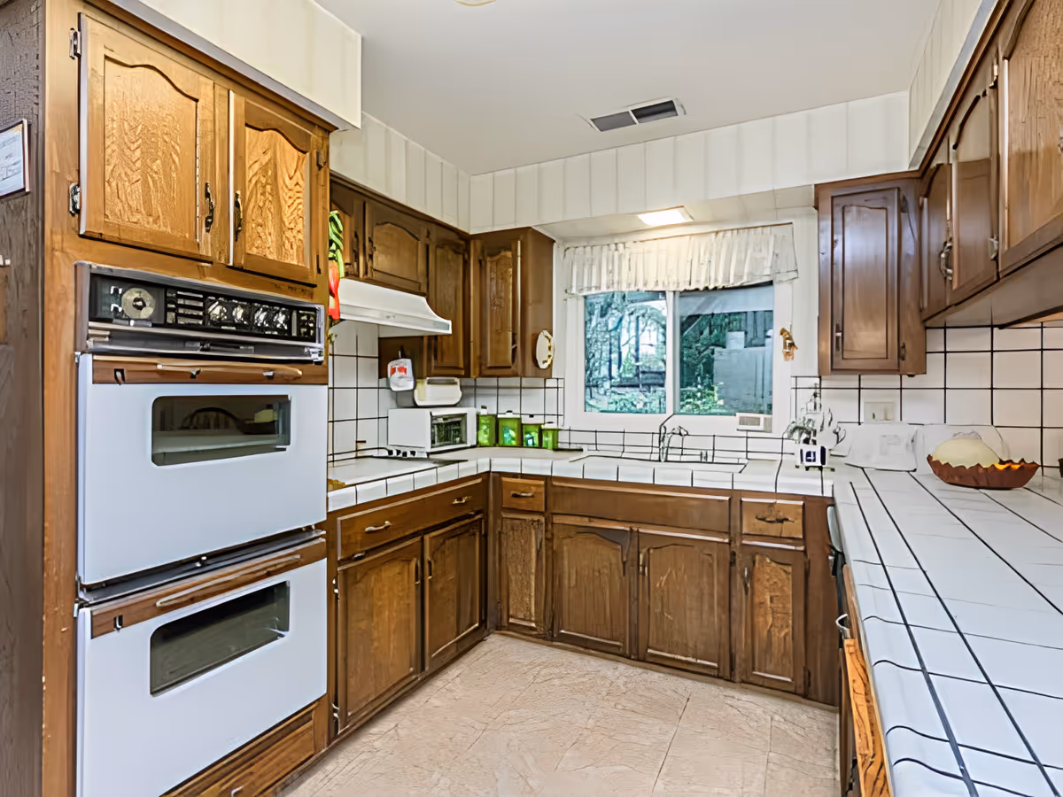 Traditional kitchen with wooden cabinets, tiled countertops, double wall ovens, and a window over the sink.