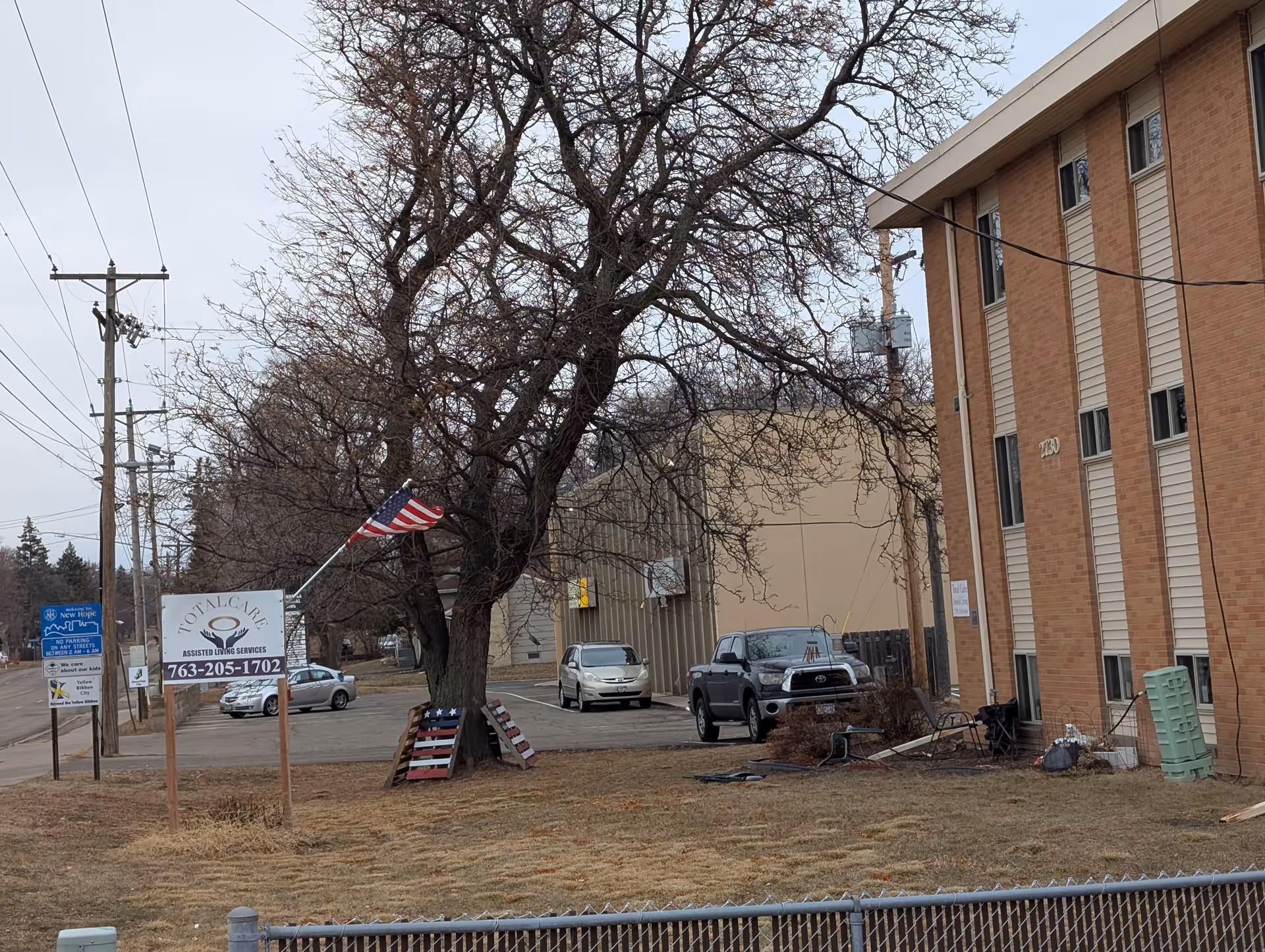 Exterior view of a multi-story brick senior living building with a front lawn, American flag, parking lot and a sign.