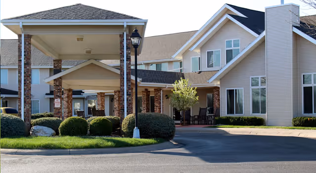 Exterior front entrance of Linden Estates showing a covered porte-cochere with brick columns, trimmed shrubs and a circular driveway.