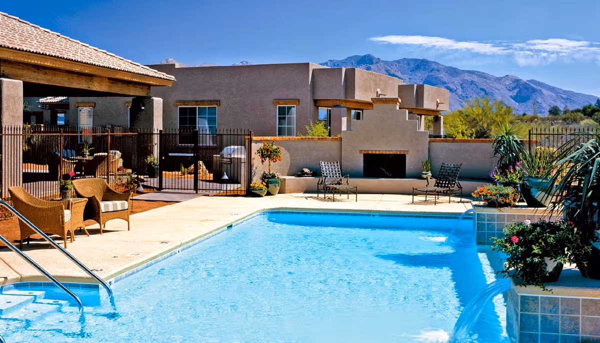 Outdoor swimming pool and patio seating in front of a southwestern-style building with mountains in the background.