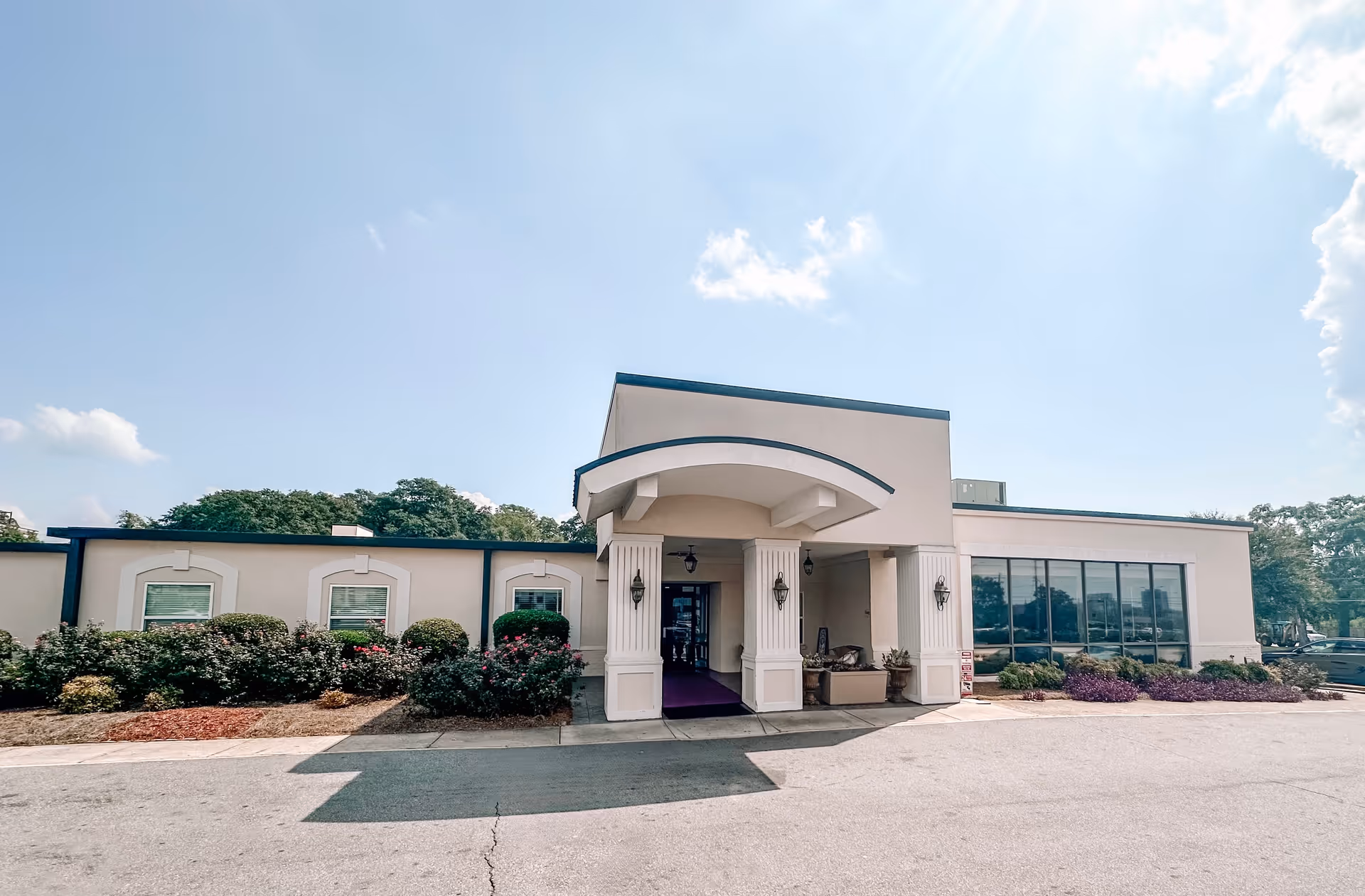 Front entrance of a single-story healthcare building with a covered porte-cochere, columns, large windows and landscaped shrubs.