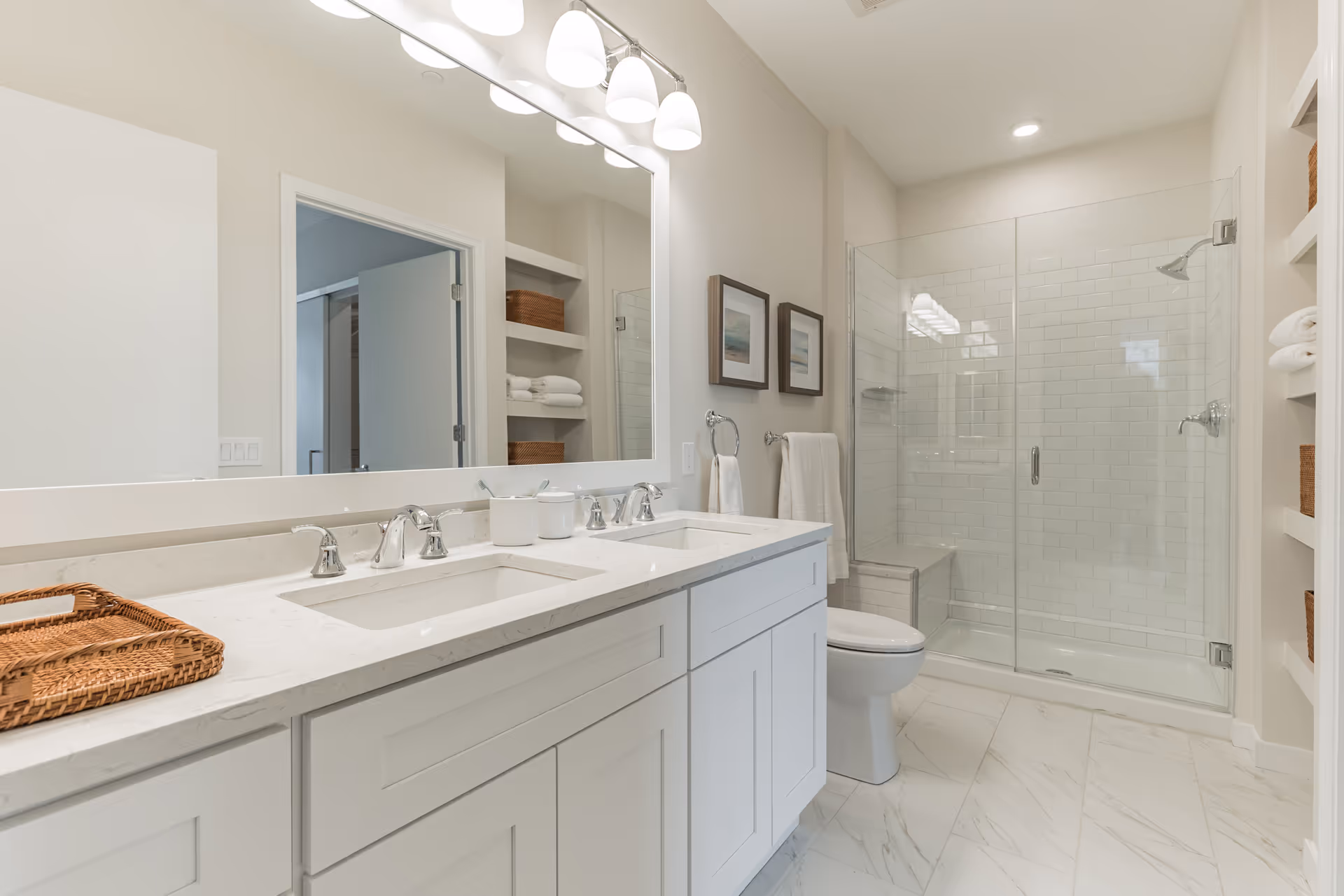 Bright, modern bathroom with a double-sink vanity, large mirror, toilet, and a glass-enclosed walk-in shower.